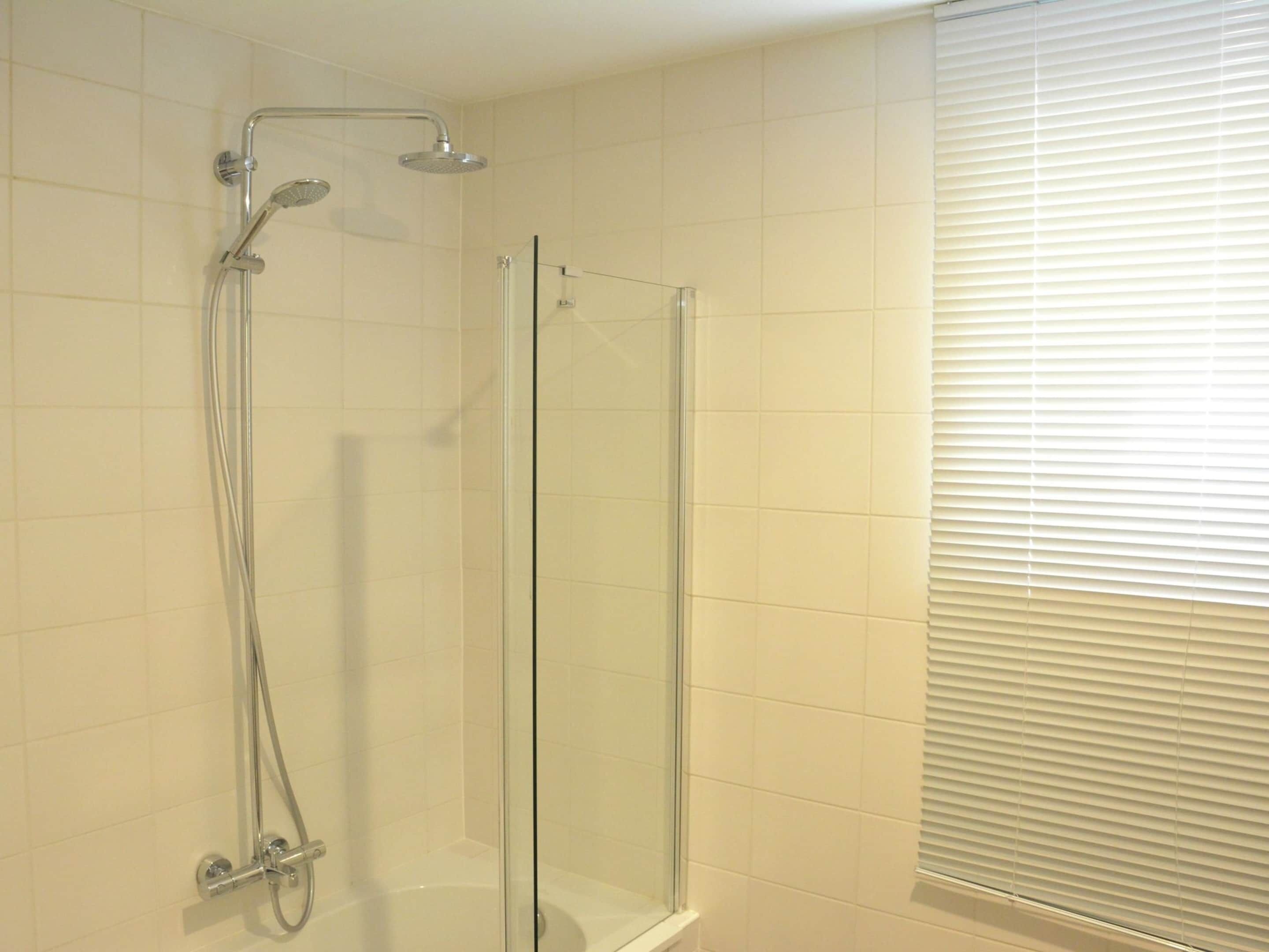 A glass-enclosed shower with a handheld showerhead and a wall-mounted faucet.