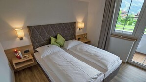 Ein Doppelbett mit weißen Bettwäsche, zwei Nachttische mit Lampen, ein Holz-Kopfteil und Blick auf Grün durch ein Fenster.