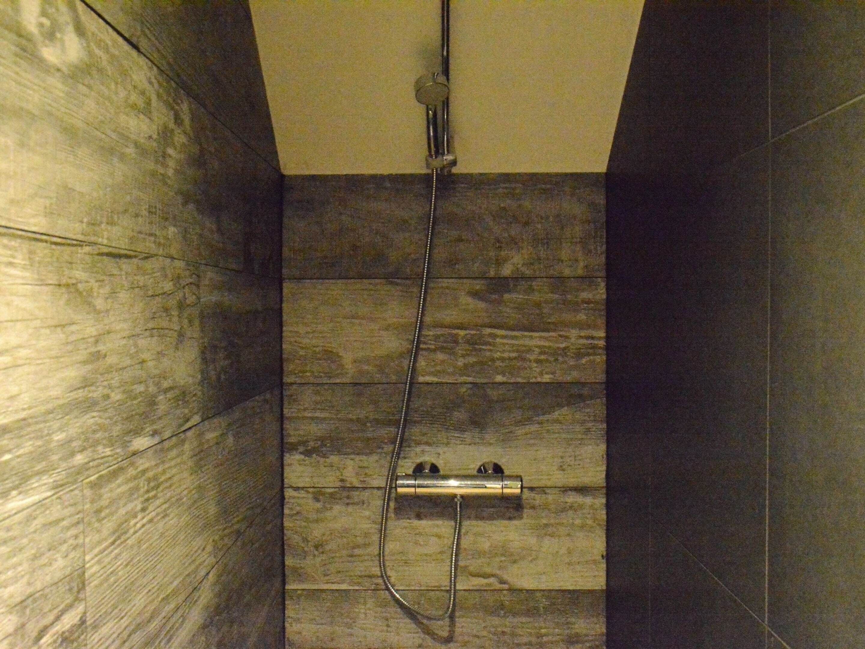 A shower with a handheld showerhead and a wall-mounted control panel.