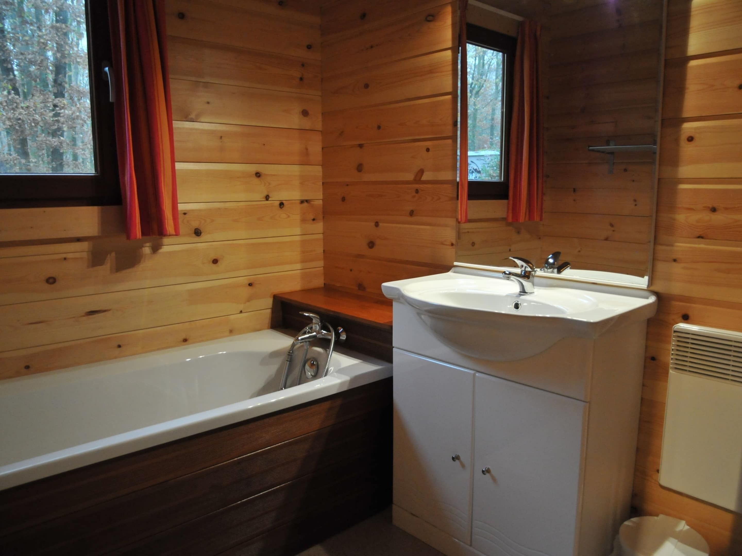 A wooden cabin bathroom with a bathtub, sink, and cabinets.