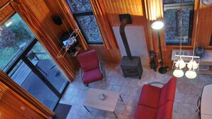 A cozy cabin interior with a fireplace, red seating, and large windows offering a view of the outdoors. - Holiday Home in Houffalize With Valley Views (Houffalize)