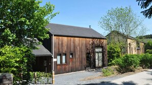 A modern building with a wooden facade, a gravel driveway, and surrounding greenery. - Holiday Home in Houffalize With Valley Views (Houffalize)