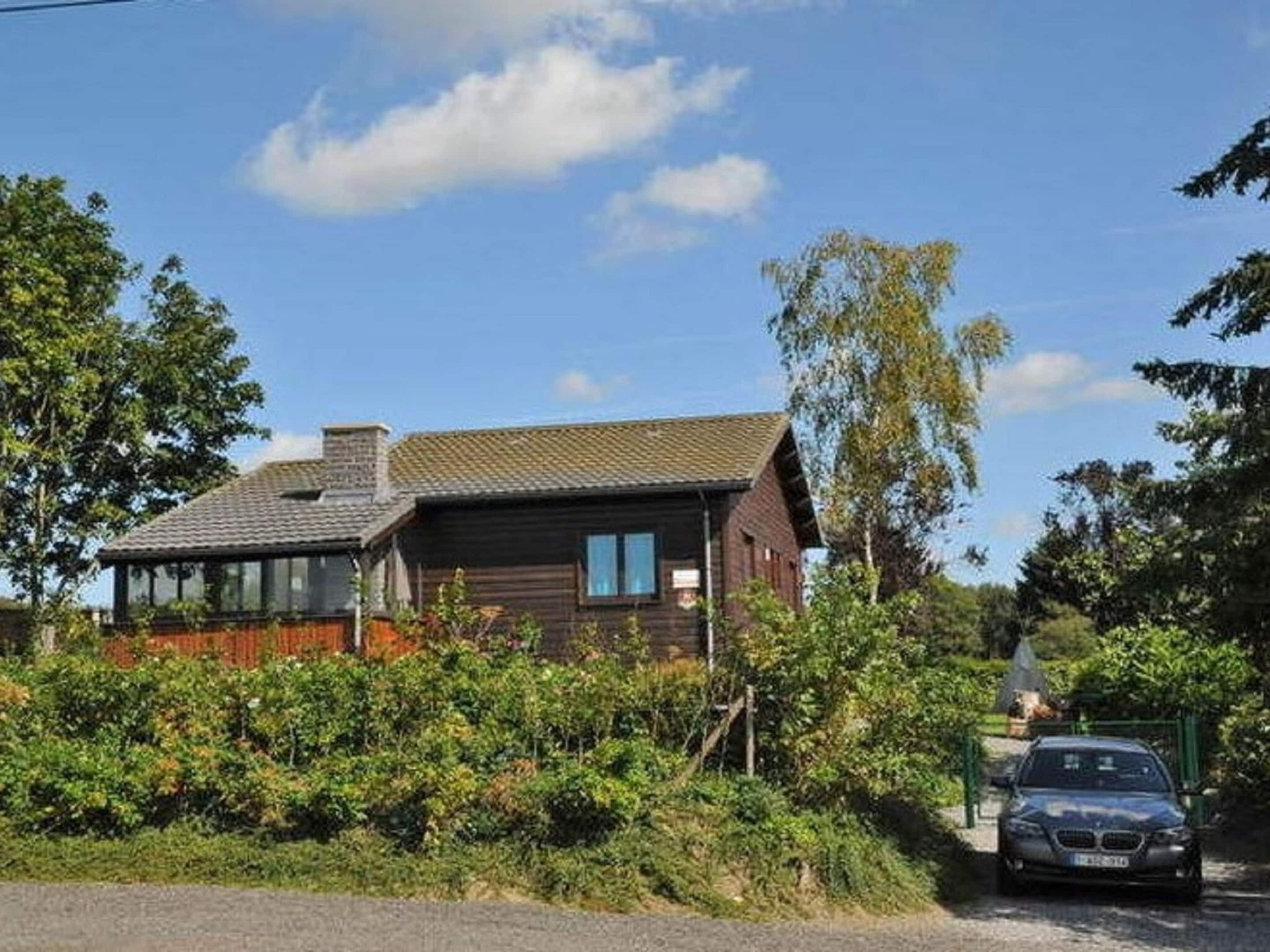 Une maison en bois avec un toit en pente, une véranda en verre et une voiture garée devant.