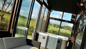 A modern outdoor seating area with a sofa and hot tub, large windows offering a view of a green landscape. - Chalet in Durbuy With Jacuzzi & Garden (Somme-Leuze)