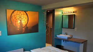 A bedroom with a bed, a bathroom with a sink and mirror, and a wall art piece. - Chalet in Durbuy With Jacuzzi & Garden (Somme-Leuze)