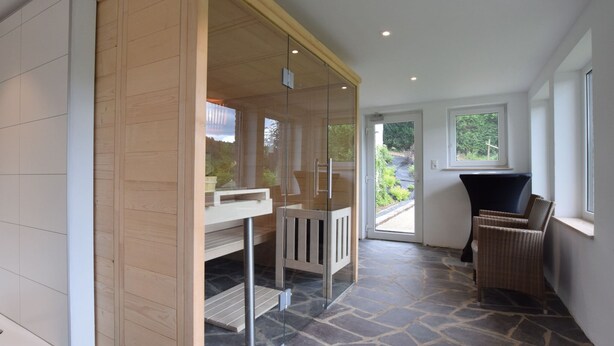 A modern room with a stone floor, a wooden partition, a white bench, and a wicker chair. - House in Vielsalm Near Tropical Pool (Vielsalm)