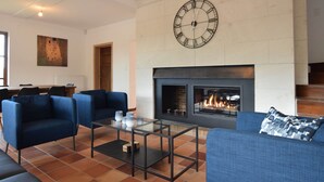A modern living room with a fireplace, blue sofas, and a large wall clock. - House in Vielsalm Near Tropical Pool (Vielsalm)