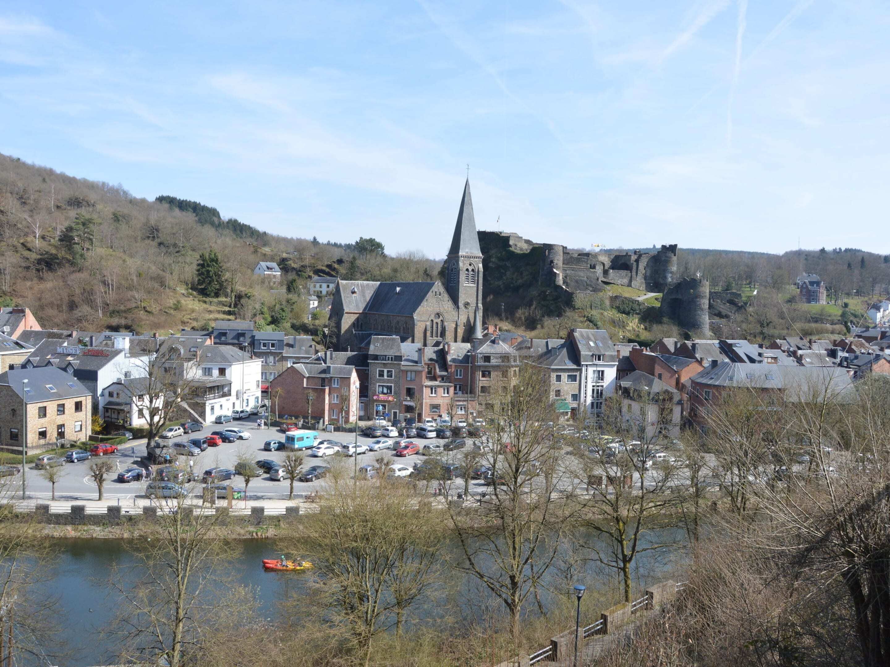 A town with a prominent church and castle on a hill, surrounded by residential buildings and a parking area with cars.