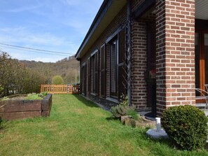 Een bakstenen gebouw met een overdekte veranda, een houten hek en een verzorgd gazon.