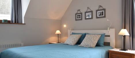 A bedroom with a bed, bedside lamps, a nightstand, a radiator, and a window with curtains.