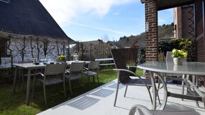 An outdoor patio with a round table and chairs, a brick wall, and a view of a residential area. - Cozy Family Holiday Home (La Roche-en-Ardenne)