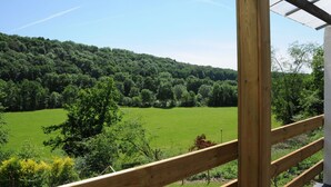 A wooden balcony with a view of a green field and forested hill. - Holiday Home in Duruby With Garden & BBQ (Durbuy)