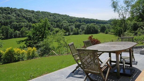 An outdoor patio with a table and chairs, overlooking a lush green landscape and forested hills. - Holiday Home in Duruby With Garden & BBQ (Durbuy)