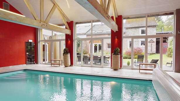 An indoor swimming pool with a red wall, wooden beams, and large windows. - Holiday Home in Trois Ponts With Private Pool (Trois-Ponts)