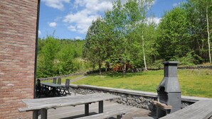 A patio area with a brick wall, picnic tables, and a stone fireplace. - Holiday Home in Barvaux With Sauna & Garden (Durbuy)