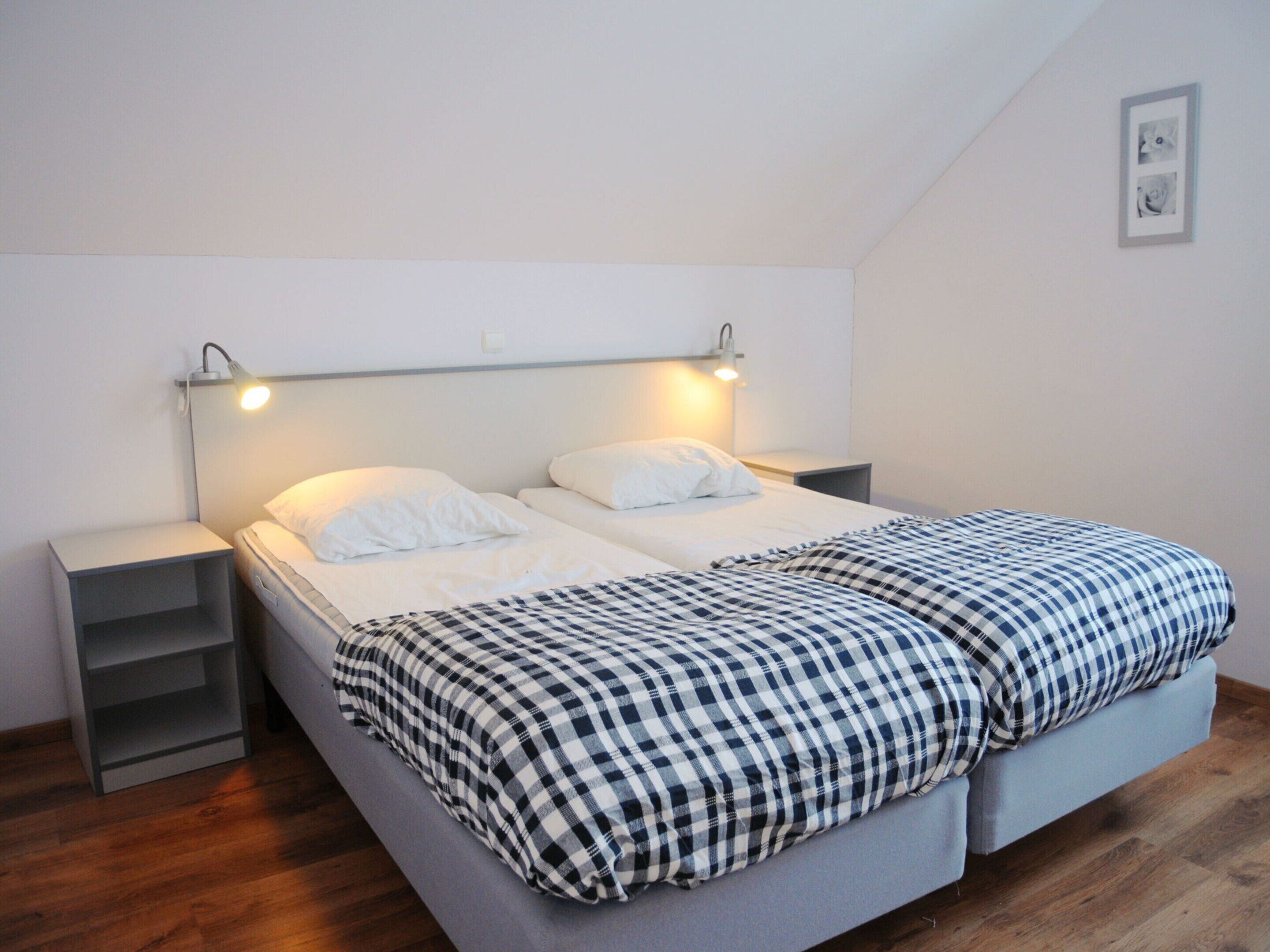 Ein Doppelbett mit kariertem Überwurf, Nachttische und Wandleuchten.