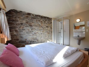 A bedroom with a stone wall, a bed with white bedding, a shower area, and a wall-mounted sink. - Luxury House with Indoor Pool, Sauna, Hot Tub (Vielsalm)