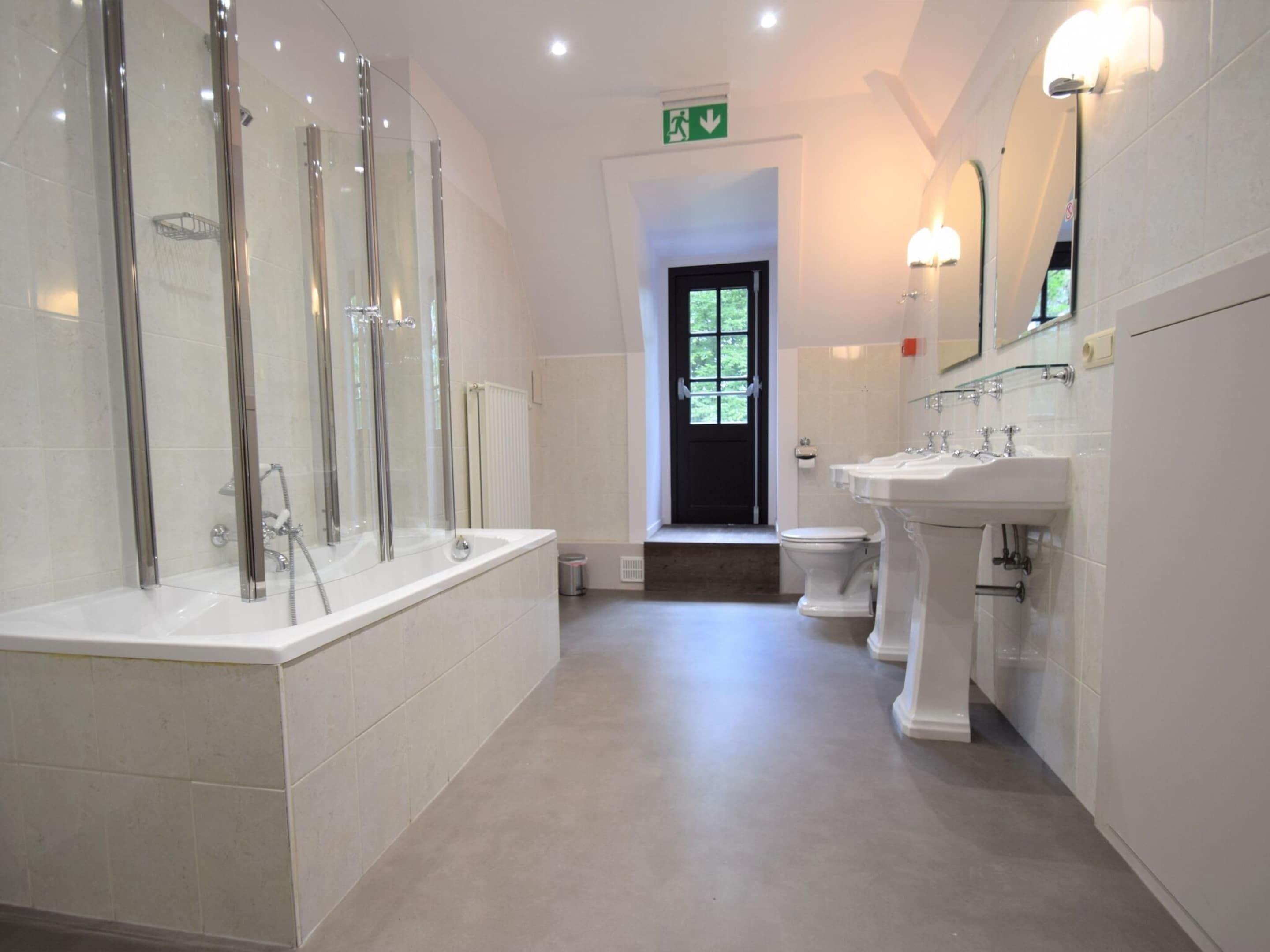 Een moderne badkamer met een douchecabine van glas, een witte wastafel en een toilet.