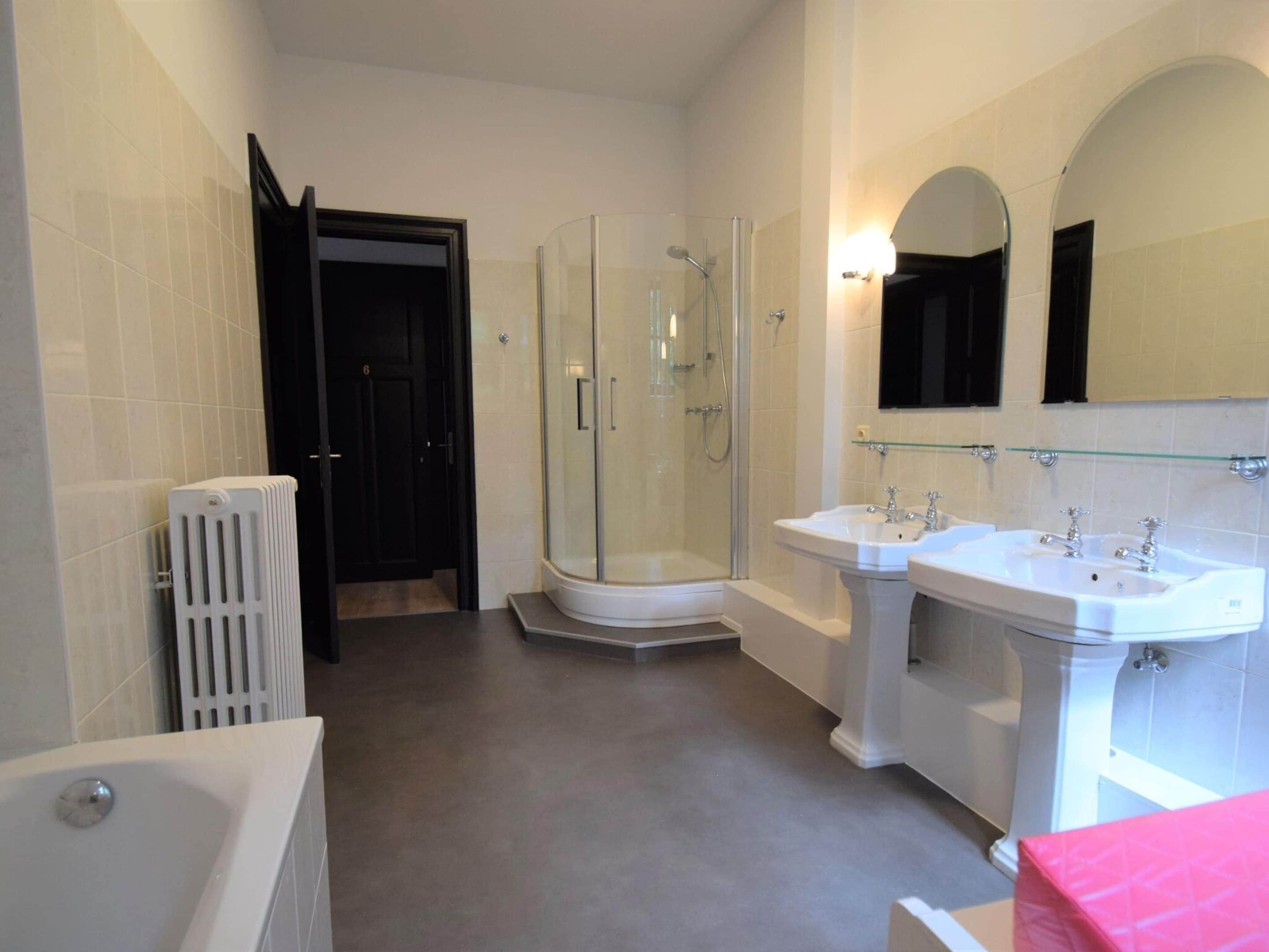 A modern bathroom with a glass-enclosed shower, two sinks, and a bathtub.