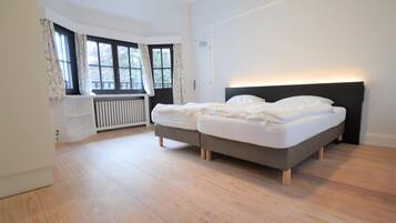 Quarto com duas camas, um radiador e janelas amplas com cortinas.