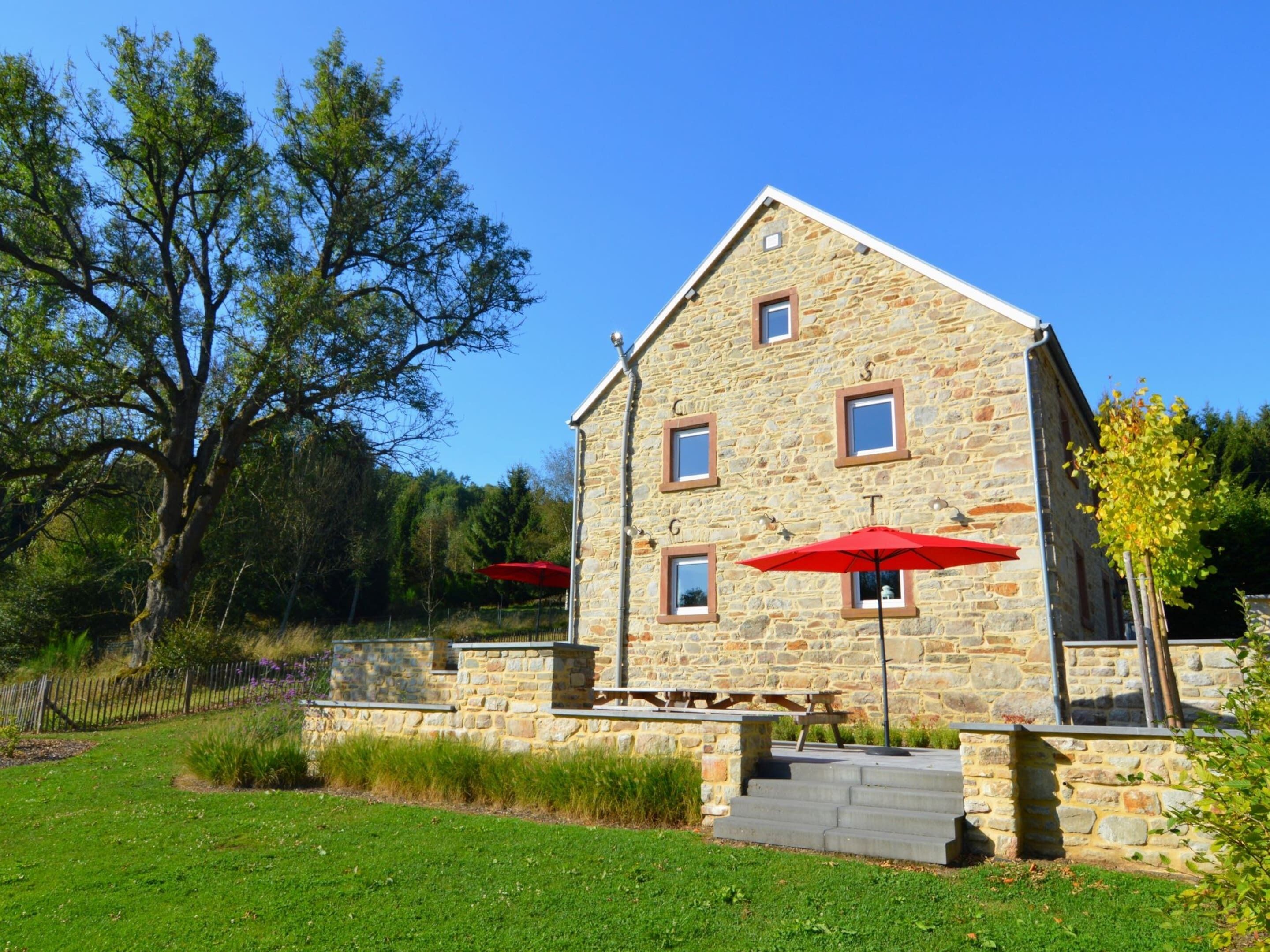 Un bâtiment en pierre avec un toit en pente, un petit porche avec des marches et deux parasols rouges.