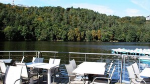 Una terraza con mesas y sillas que da a un lago, rodeada de un bosque denso.