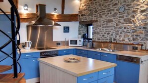 Una cocina moderna con armarios azules, una isla central, un muro de piedra y una campana extractora de acero inoxidable.