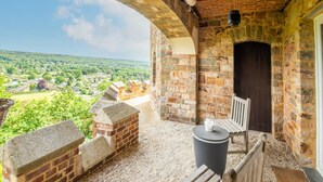 A stone-walled balcony with a wooden bench and table, a door, and a view of a green landscape. - Impressive Castle in Spa With a Swimming Pool (Jalhay)
