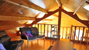 Une pièce mansardée chaleureuse avec un plafond en bois, un canapé, un fauteuil et une table.