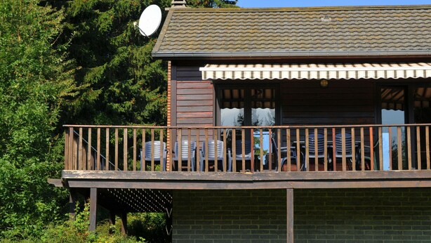 Une cabane en bois dotée d’un balcon, entourée d’arbres.