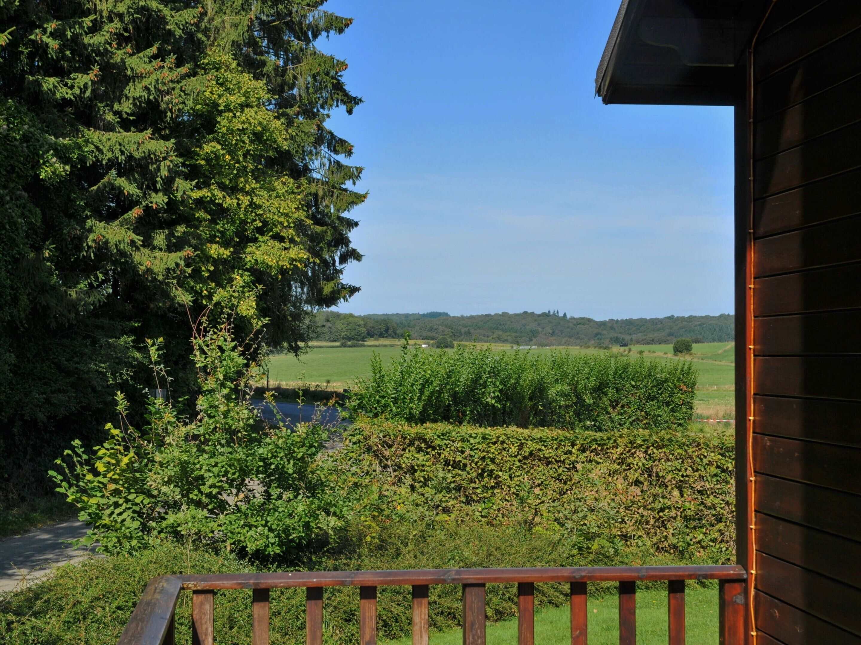 A wooden balcony overlooking a lush green landscape with a river and distant hills.
