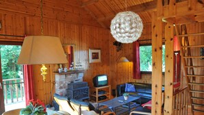 Un intérieur de chalet chaleureux avec une cheminée, des murs en bois, un téléviseur, un canapé et un coin repas.