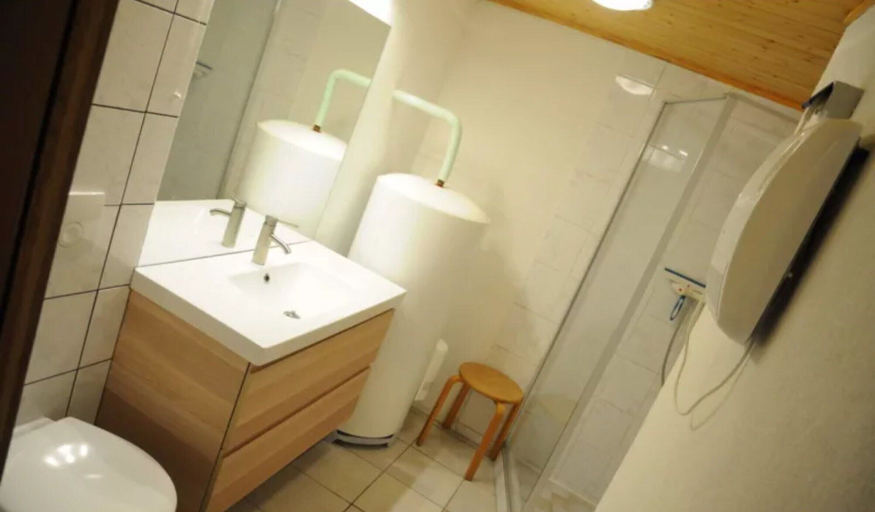 A bathroom with a white sink, wooden vanity, and a small stool.