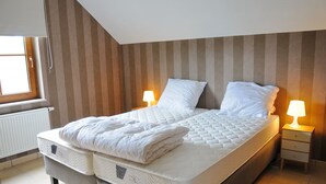 Un lit double bien fait, avec un matelas matelassé, deux lampes de chevet et une fenêtre équipée de stores.