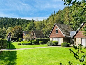 A row of traditional wooden houses with stone foundations, surrounded by well-maintained lawns and dense forest in the background. - Cottage Famille - Family Resort With Wellness in the Heart of the Ardennes (Malmedy)