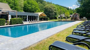 A swimming pool with lounge chairs, a covered area, and a forested hillside in the background. - Cottage Famille - Family Resort With Wellness in the Heart of the Ardennes (Malmedy)