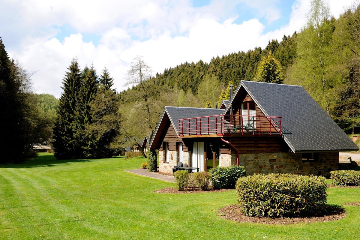 A lodge with a stone exterior, a balcony with a red railing, and a well-maintained lawn.