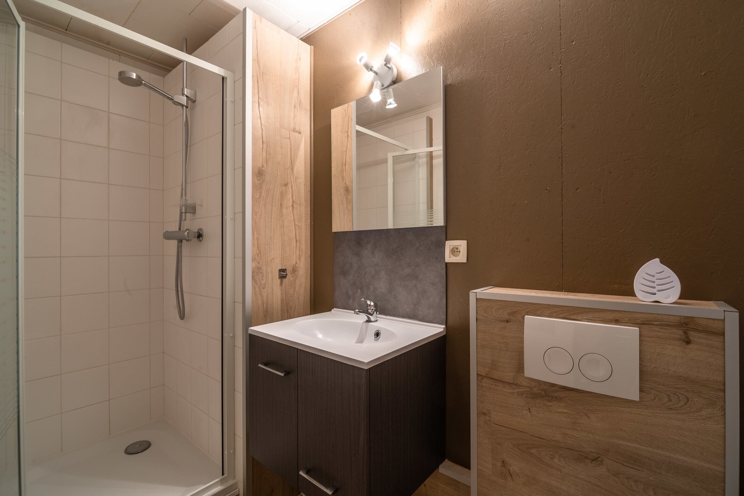 Ein Badezimmer mit Dusche, Waschbecken, Holzkästen und einem beleuchteten Spiegel.