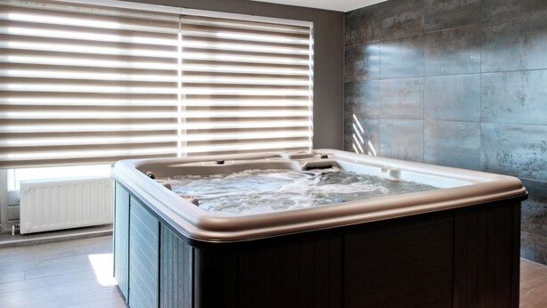 A modern bathroom with a hot tub, large windows with blinds, and a tiled wall. - Swanky Holiday Home in Waimes With Indoor Swimming Pool (Waimes)
