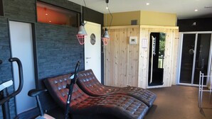 A massage chair, exercise bike, and a wooden wall with a sliding door. - Swanky Holiday Home in Waimes With Indoor Swimming Pool (Waimes)