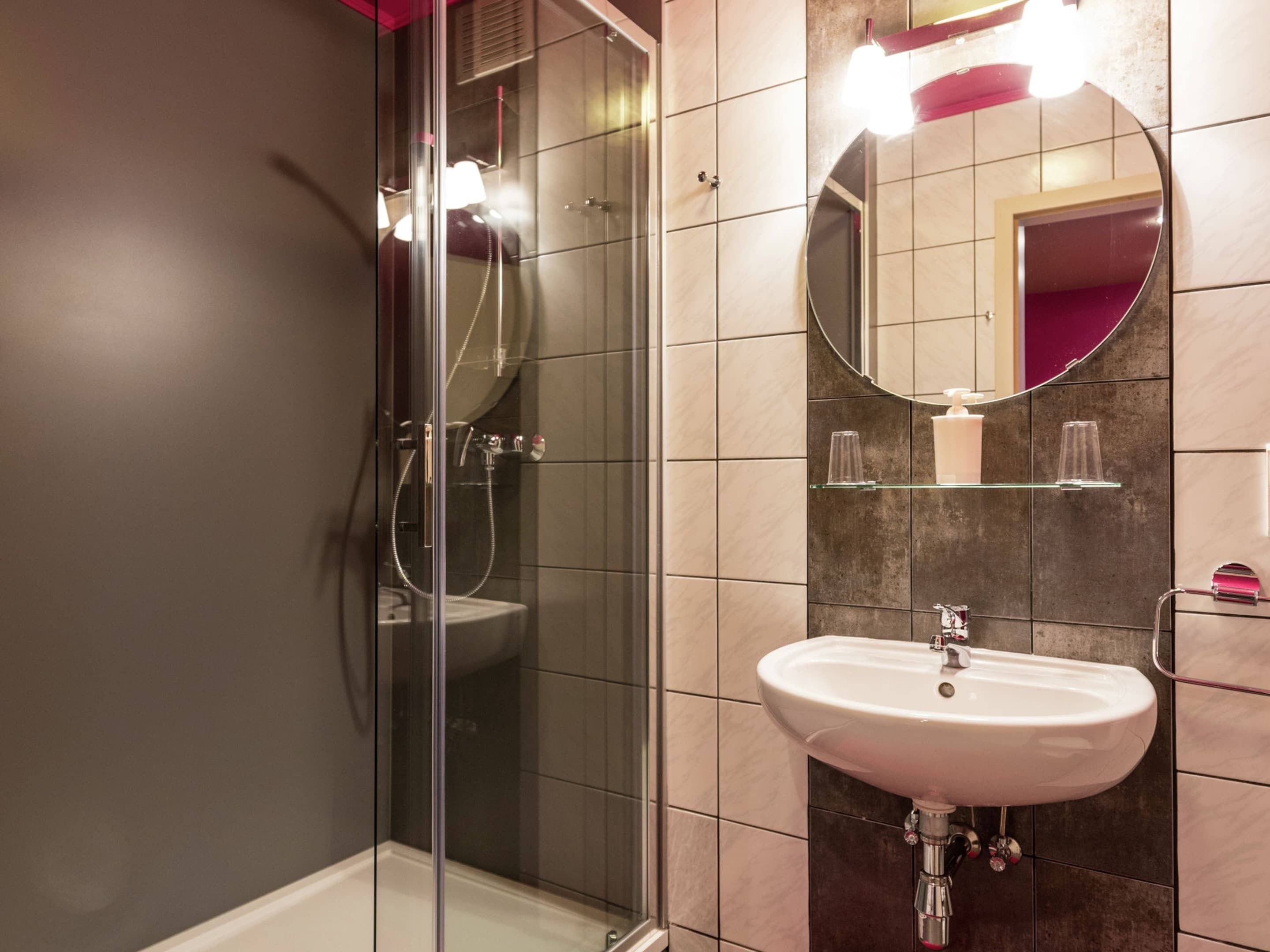 A modern bathroom with a glass shower enclosure, a white sink, and a mirror.