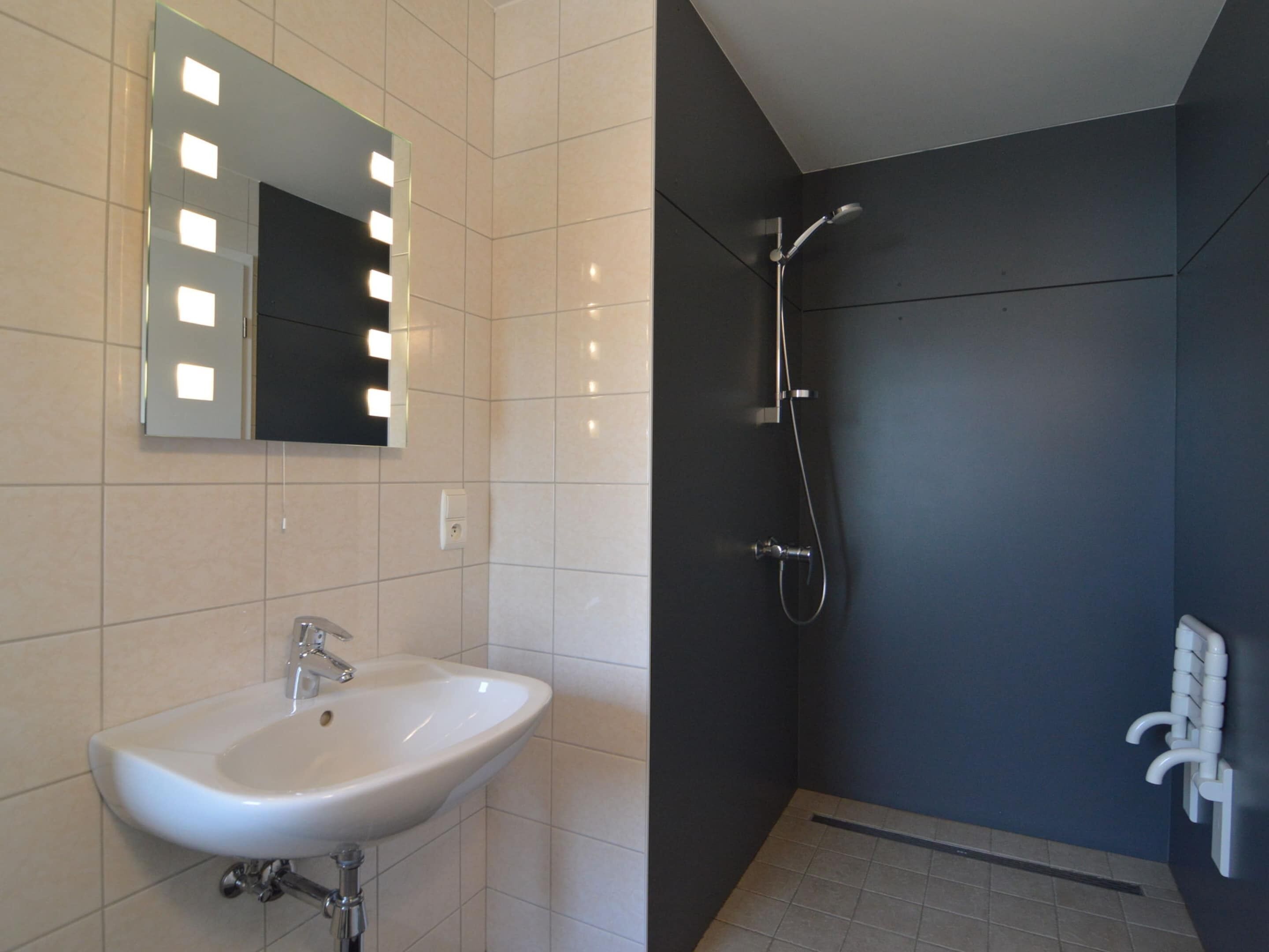 A bathroom with a white sink, a mirror with lights, and a shower.