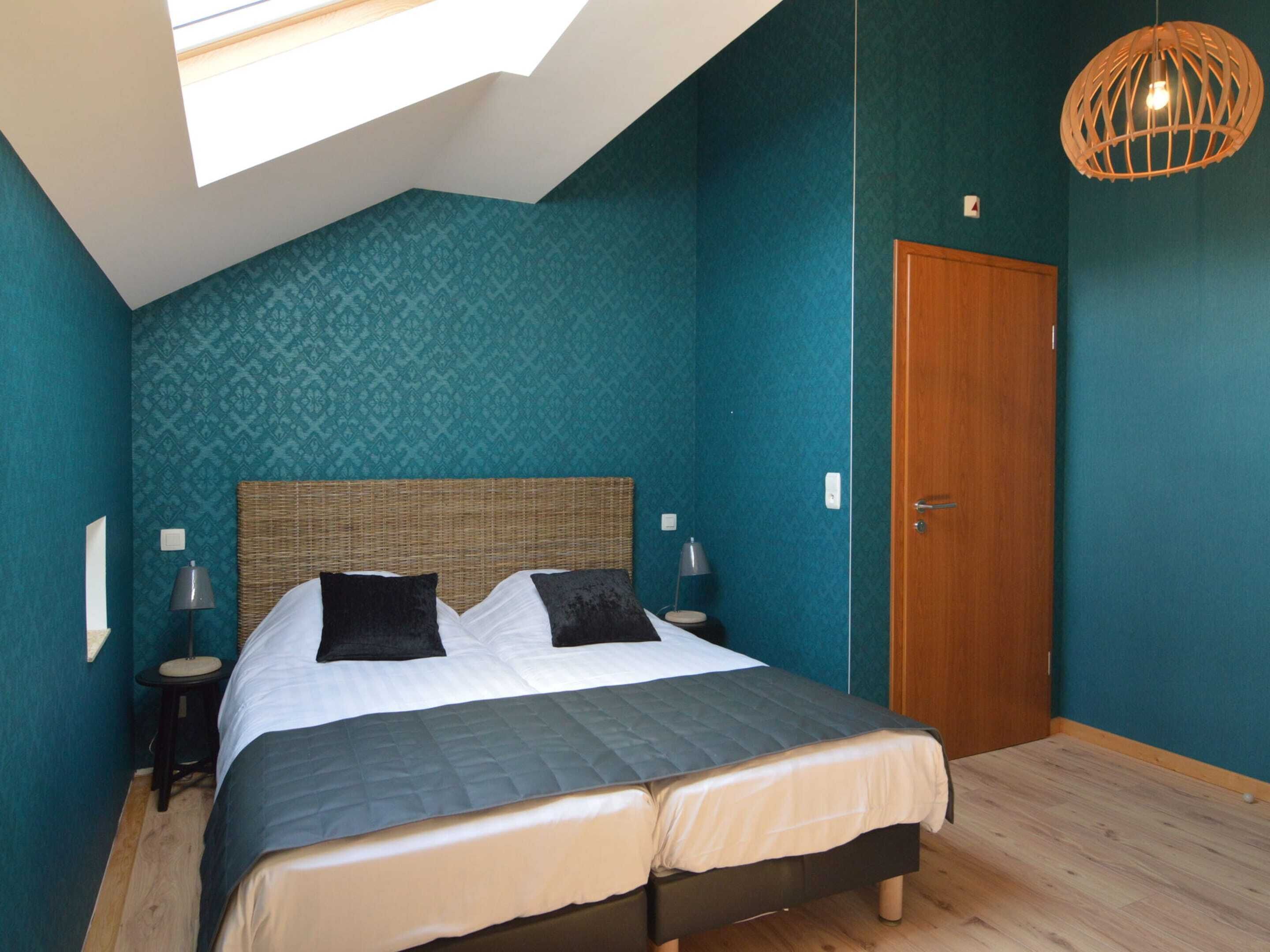 Quarto com uma cama grande, porta de madeira e claraboia.