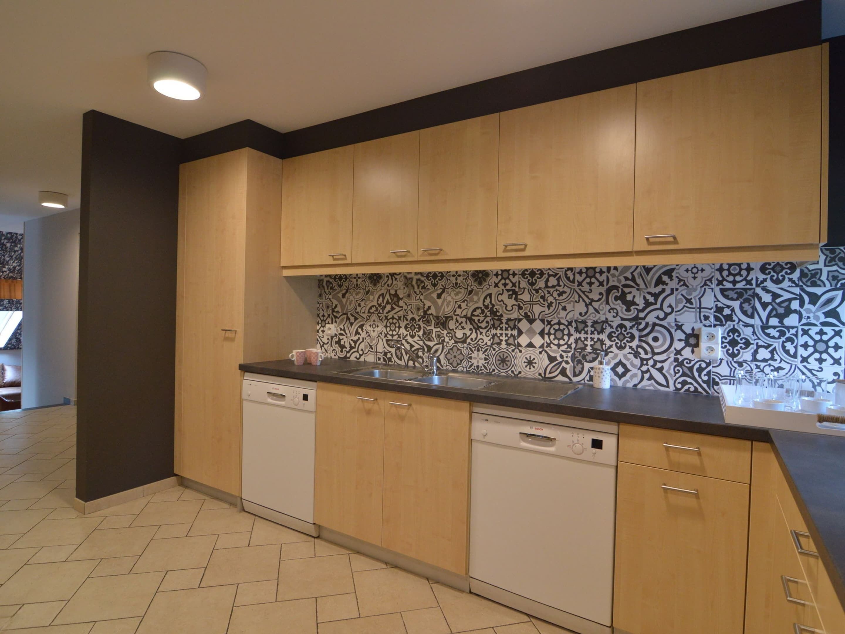 A modern kitchen with wooden cabinets, a dishwasher, and a patterned backsplash.