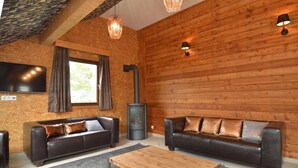 Ein gemütliches Wohnzimmer mit zwei Ledersofas, einem Holztisch, einem Kamin und einem an der Wand befestigten Fernseher.