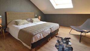 Ein Schlafzimmer mit schrägen Wänden, einem großen Bett mit gewebtem Kopfteil, zwei Nachttischlampen, einem Sessel und einem Teppich.
