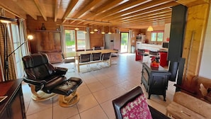 A spacious room with a wooden ceiling, a dining table, chairs, a sofa, and a fireplace. - Chalet Near Hampteau (Hotton)