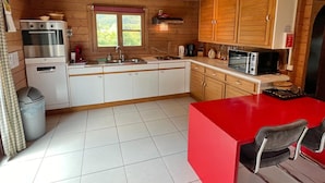 A compact kitchen with wooden cabinets, a red countertop, a sink, a microwave, and a small oven. - Chalet Near Hampteau (Hotton)