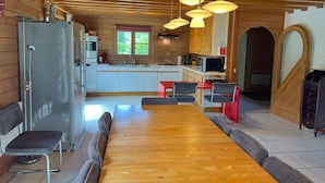 A wooden cabin interior with a dining area, kitchen, and a large window. - Chalet Near Hampteau (Hotton)