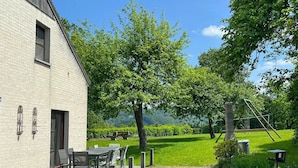 A building with a brick exterior, outdoor seating area with tables and chairs, and a swing set in a grassy area. - Chalet Near Hampteau (Hotton)